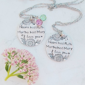 Może przedstawiać: Dwa srebrne naszyjniki z wisiorkami z motywami kwiatowymi i napisem "Naomi had Ruth, Martha had Mary, I have you." Każdy wisiorek ma kamień szlachetny. Jeden ma r&oacute;żowe i zielone kamienie. Drugi ma zielony kamień.