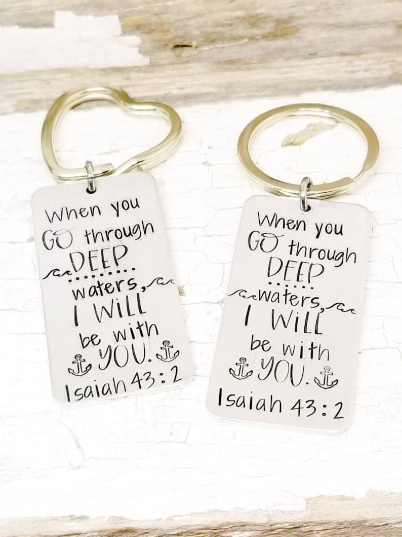 May include: Two silver keychains with heart and circle rings. Each keychain has a rectangular tag with the text "When you go through deep waters, I will be with you. Isaiah 43:2" and an anchor symbol.