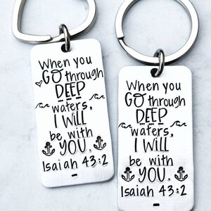 May include: Two silver keychains with heart-shaped rings. Each keychain has a rectangular tag with the text "When you go through deep waters, I will be with you. Isaiah 43:2" and an anchor symbol.