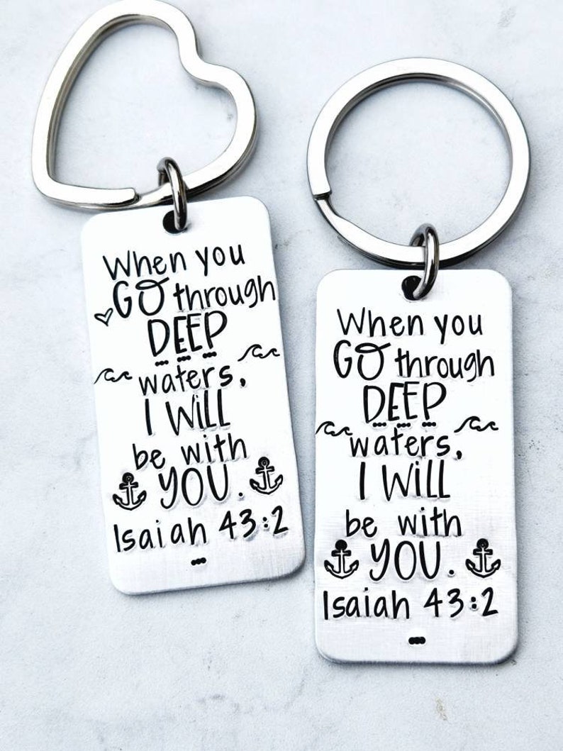 May include: Two silver keychains with heart-shaped rings. Each keychain has a rectangular tag with the text "When you go through deep waters, I will be with you. Isaiah 43:2" and an anchor symbol.
