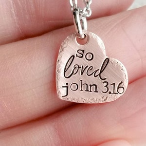 May include: A silver chain necklace with a copper heart pendant that says "so loved john 3:16".