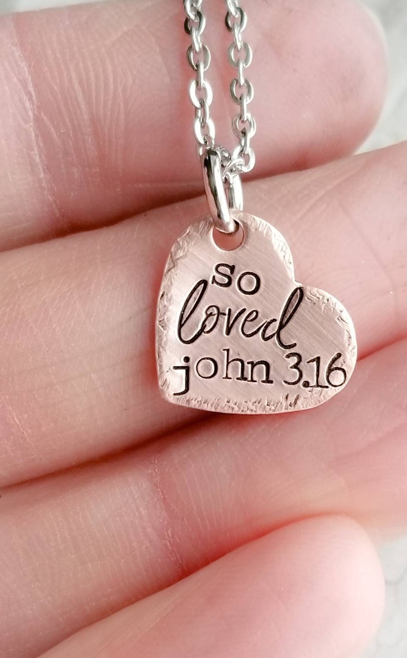 May include: A silver chain necklace with a copper heart pendant that says "so loved john 3:16".