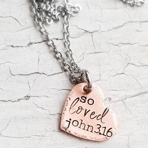 May include: A silver chain necklace with a copper heart pendant that says "so loved john 3:16".
