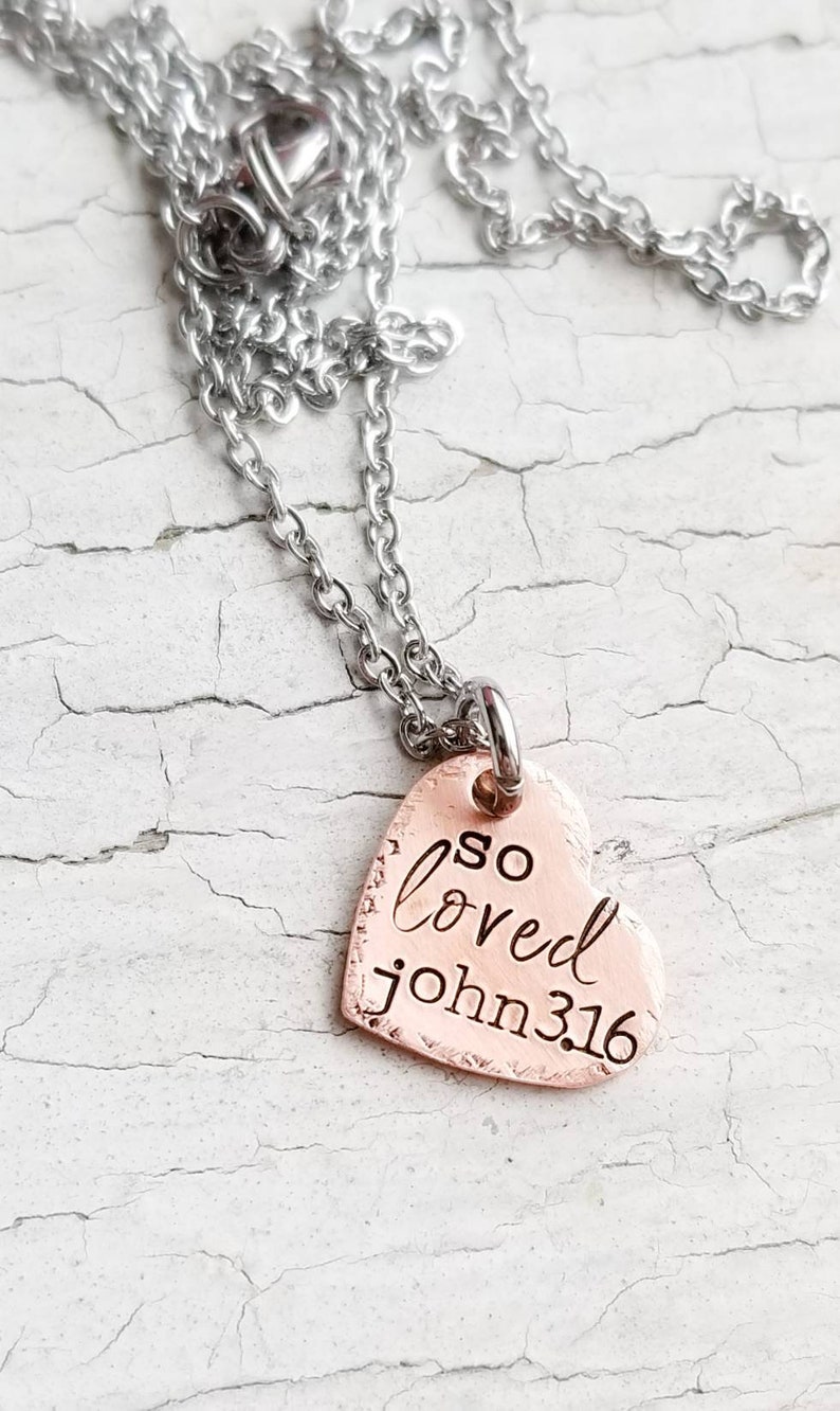 May include: A silver chain necklace with a copper heart pendant that says "so loved john 3:16".