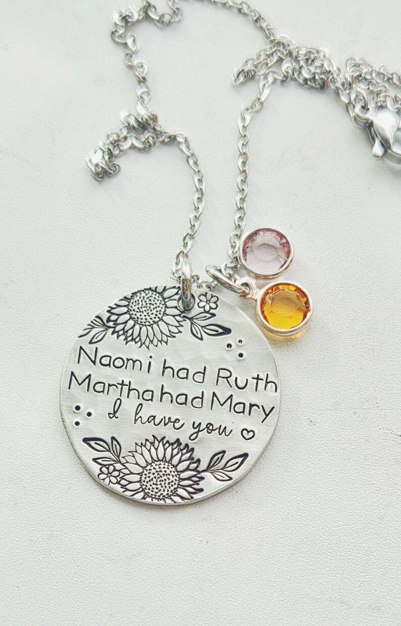 Może przedstawiać: Srebrny naszyjnik z wisiorkiem z okrągłym urokiem z wygrawerowanym tekstem i kwiatowymi wzorami. Tekst brzmi "Naomi had Ruth Martha had Mary... I have you." Dwa urocze kamienie szlachetne, jeden r&oacute;żowy i jeden ż&oacute;łty, zwisają z łańcuszka.