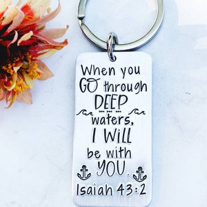 May include: Silver keychain with the text "When you go through deep waters, I will be with you. Isaiah 43:2" and two anchor symbols.