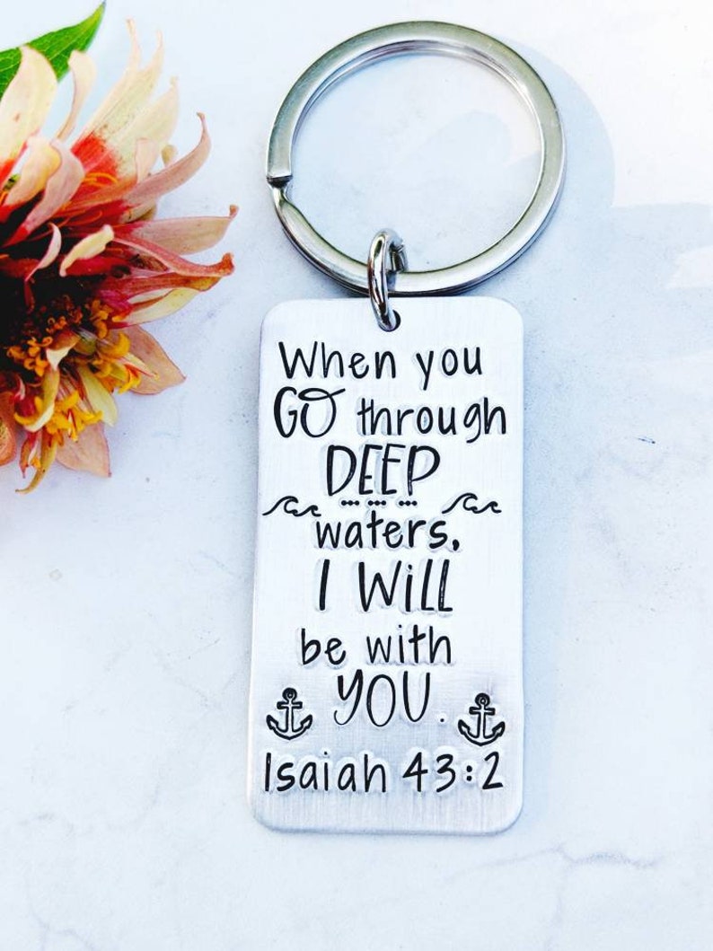 May include: Silver keychain with the text "When you go through deep waters, I will be with you. Isaiah 43:2" and two anchor symbols.
