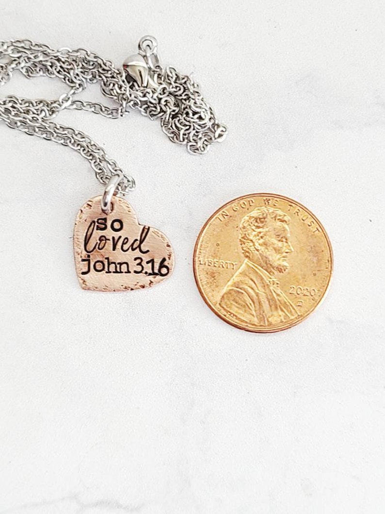 May include: A silver chain necklace with a copper heart pendant that says "so loved John 3:16".