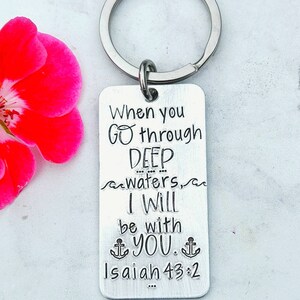 May include: Silver keychain with a rectangular tag that reads "When you go through DEEP waters, I WILL be with YOU. Isaiah 43:2". The tag has a wavy line above and below the word "waters" and two anchor symbols on either side of the word "YOU".