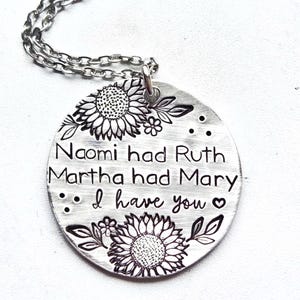 Może przedstawiać: Srebrny naszyjnik z okrągłą zawieszką. Zawieszka zawiera wygrawerowany tekst i ilustracje słonecznik&oacute;w. Tekst brzmi: "Naomi had Ruth, Martha had Mary, I have you".