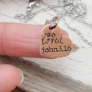 May include: A copper heart-shaped pendant necklace with the words "so loved john 3.16" engraved on it.