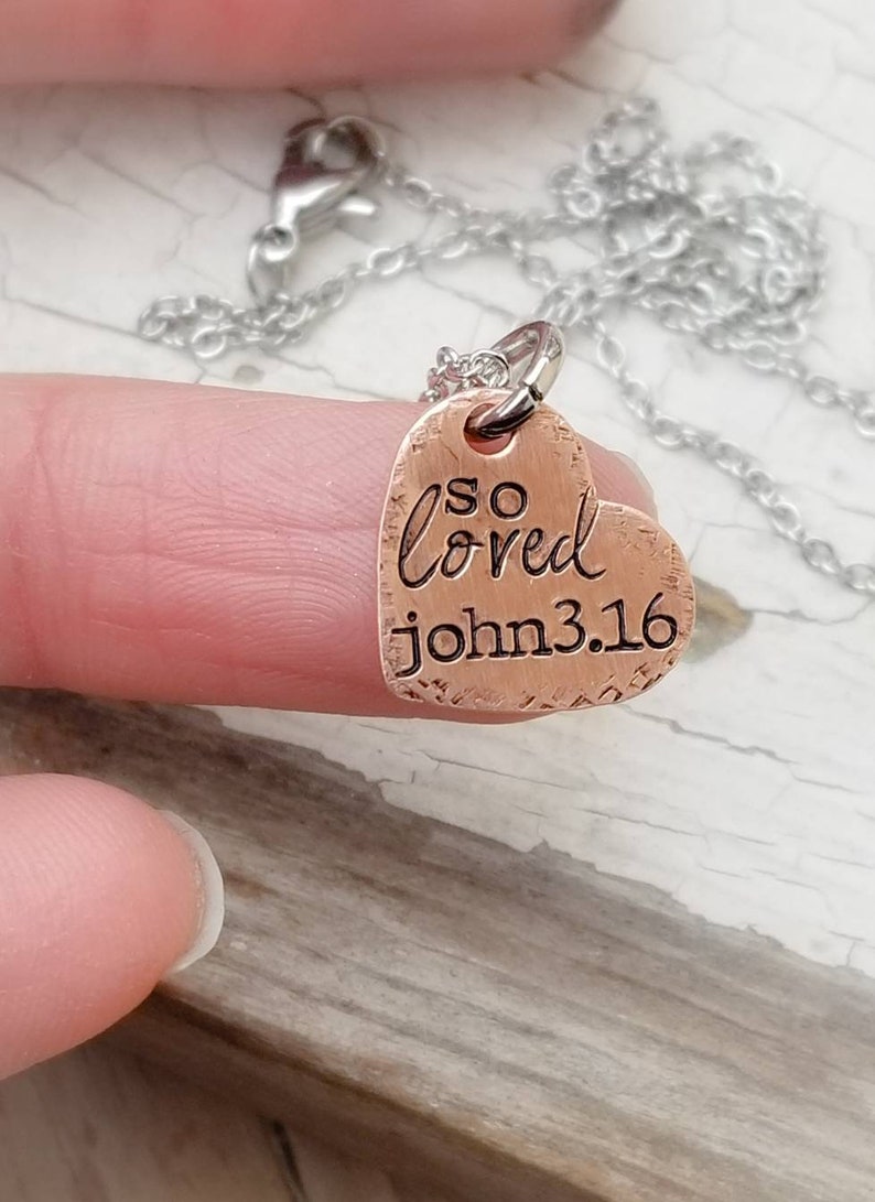 May include: A copper heart-shaped pendant necklace with the words "so loved john 3.16" engraved on it.