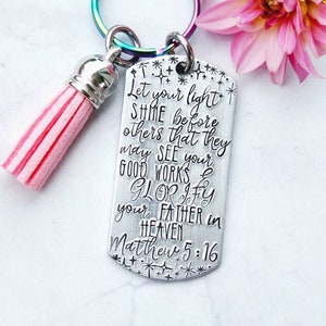 May include: A silver keychain with a pink tassel. The keychain has a quote from the Bible, Matthew 5:16, "Let your light shine before others that they may see your good works and glorify your Father in heaven."