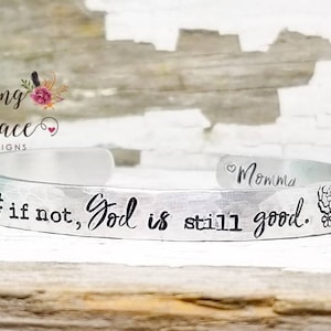 May include: Silver cuff bracelet with the words "if not, God is still good." and a floral design. The bracelet is personalized with the word "Momma".