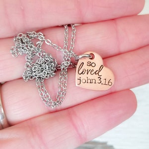 May include: A silver chain necklace with a copper heart pendant that says "so loved john 3:16".