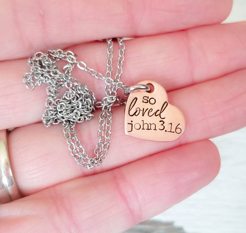 May include: A silver chain necklace with a copper heart pendant that says "so loved john 3:16".
