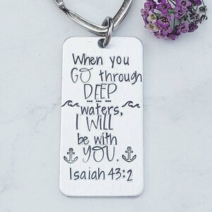 May include: Silver keychain with a heart-shaped ring and a rectangular tag. The tag has the text "When you go through DEEP waters, I WILL be with YOU. Isaiah 43:2" engraved on it.