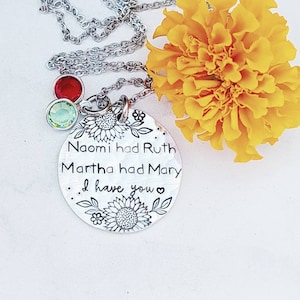 Może przedstawiać: Srebrny naszyjnik z okrągłą zawieszką z wygrawerowanym tekstem i kwiatowymi wzorami. Na zawieszce widnieje napis "Naomi had Ruth, Martha had Mary, I have you". Dwa urocze kamienie szlachetne w kolorze czerwonym i zielonym zwisają z łańcuszka. Ż&oacute;łty kwiat w tle.