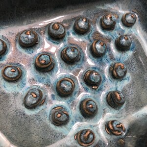May include: A blue and brown ceramic dish with a textured surface. The dish has a series of raised circles, creating a unique design.