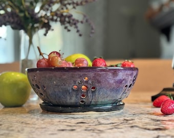 Könnte beinhalten: Eine violette und blaue Keramik-Obstschale mit einem dekorativen Design aus kleinen Kreisen. Die Schale hat einen abnehmbaren Boden und ist mit Trauben, Äpfeln und Erdbeeren gefüllt.