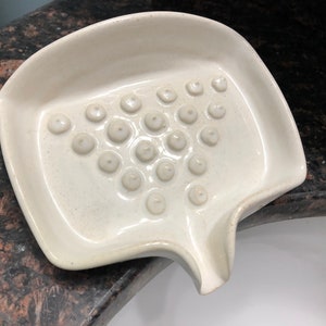May include: White ceramic soap dish with a raised, textured surface and a small spout for draining water.