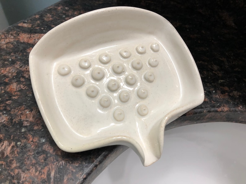 May include: White ceramic soap dish with a raised, textured surface and a small spout for draining water.