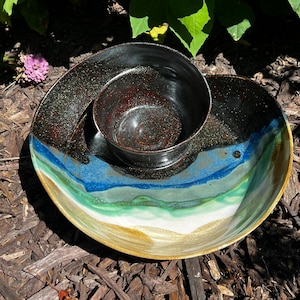 May include: A ceramic serving dish with a black and blue glaze. The dish has a smaller bowl in the center with a black and brown glaze. The dish is perfect for serving dips and snacks.