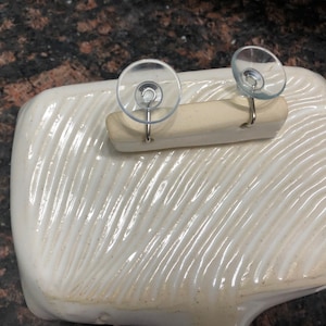 May include: White ceramic dish with a textured surface. Two suction cups with hooks are attached to a wooden bar, which is placed on top of the dish.