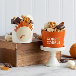 K&ouml;nnte beinhalten: Zwei Papierbecher gef&uuml;llt mit einer Mischung aus Brezeln, Schokoladenbonbons und wei&szlig;en Schokoladenst&uuml;ckchen. Ein Becher ist mit einem Truthahn-Design und dem Text "Gobble Gobble" verziert. Der andere Becher ist mit einem Truthahn-Design und dem Text "Gobble Gobble" verziert.