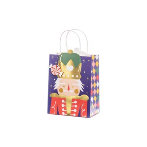 May include: A small gift bag featuring a cartoon nutcracker design. The bag has a purple background with a diamond pattern on the sides. The nutcracker has a gold crown and red uniform. A candy ornament hangs from the handle.