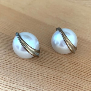 May include: A pair of white pearl earrings with a gold metal band around each pearl.