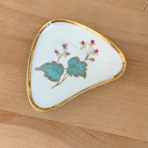 May include: A white ceramic dish with a gold rim and a floral design. The flowers are pink and the leaves are teal.