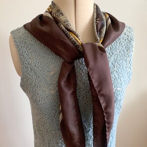 May include: A brown silk scarf with a geometric pattern in yellow and black. The scarf is tied around a mannequin's neck.