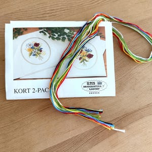 以下が含まれることがあります： 花柄のデザインのクロスステッチキット。 キットには、花の刺繍模様の白いカード、カラフルな刺繍糸、および「KORT 2-PAC」のテキストが含まれています。 ブランド名「ILTEX BRODERISTUGA SJUNTORP SWEDEN」も表示されています。