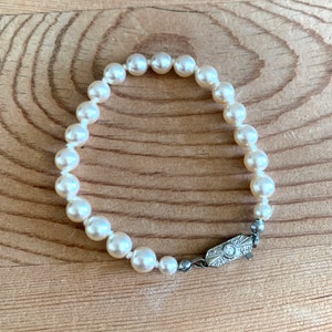 May include: A white pearl bracelet with a silver clasp. The clasp has a small diamond in the center.