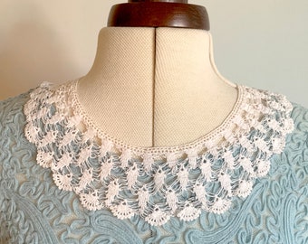 May include: A light blue dress with a white, crocheted collar. The dress is displayed on a mannequin. The collar is a delicate, openwork design. The dress has a textured pattern.