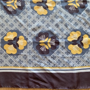 May include: A gray and white fabric with a repeating pattern of yellow and brown flowers. The fabric has a gray border with a white and yellow stripe.