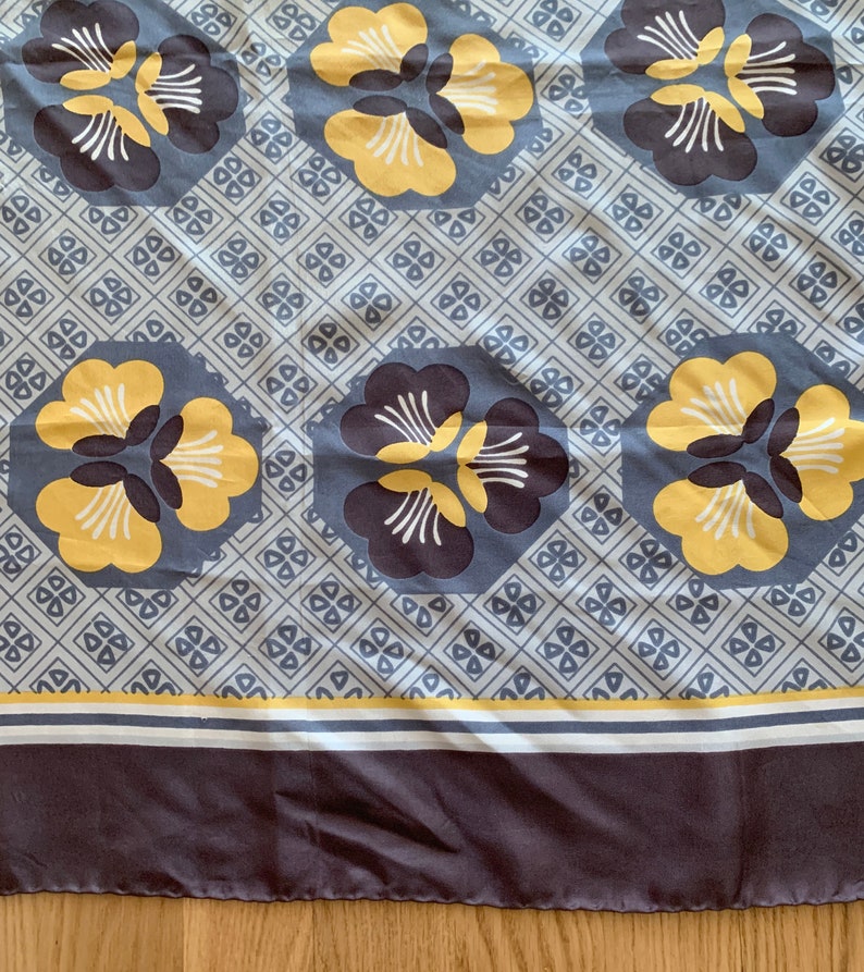 May include: A gray and white fabric with a repeating pattern of yellow and brown flowers. The fabric has a gray border with a white and yellow stripe.