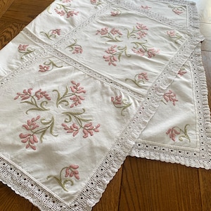 Può includere: Tovaglia bianca con ricamo floreale delicato rosa e verde e un bordo in pizzo all'uncinetto.