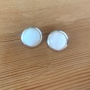 Puede incluir: Un par de pendientes redondos blancos con engastes plateados.