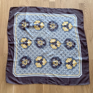 May include: A dark gray silk scarf with a white and yellow floral pattern. The pattern features stylized flowers with yellow centers and white petals.