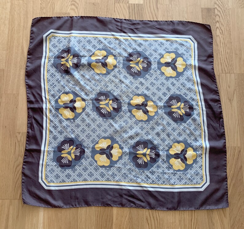 May include: A dark gray silk scarf with a white and yellow floral pattern. The pattern features stylized flowers with yellow centers and white petals.