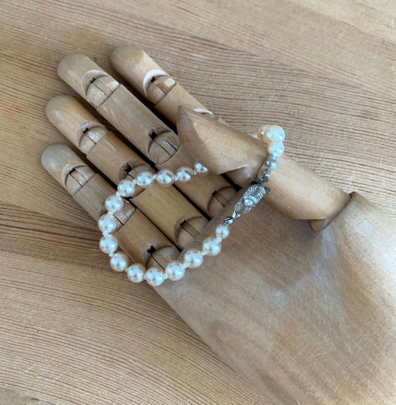 May include: A white pearl bracelet with a silver clasp. The bracelet is on a wooden hand model.