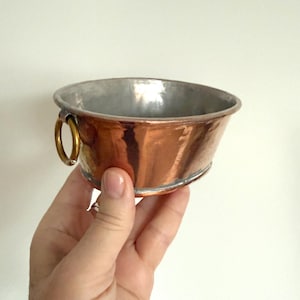 Könnte beinhalten: Eine weiße Keramiktasse mit schwarzem Henkel und dem Text "But First, Coffee" in schwarzer, handschriftlicher Schrift. Die Tasse steht auf einer weißen Oberfläche.