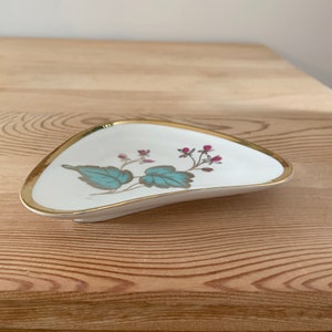 May include: A white ceramic trinket dish with a gold rim and a floral design featuring teal leaves and pink flowers.