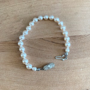 May include: A white pearl bracelet with a silver clasp. The clasp has a small diamond in the center.