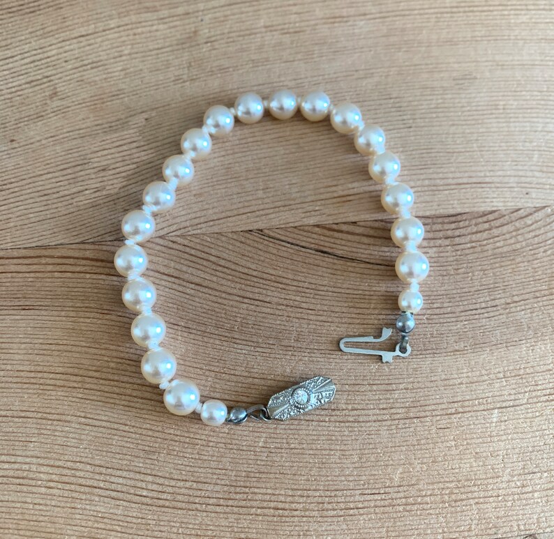 May include: A white pearl bracelet with a silver clasp. The clasp has a small diamond in the center.
