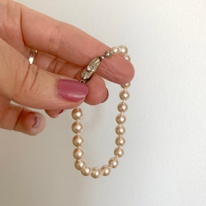 May include: A white pearl bracelet with a silver clasp featuring a small diamond. The bracelet is held in a hand with pink nail polish.