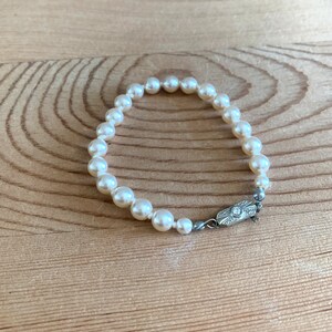 May include: A white pearl bracelet with a silver clasp. The bracelet is made of small, round pearls and has a simple design.
