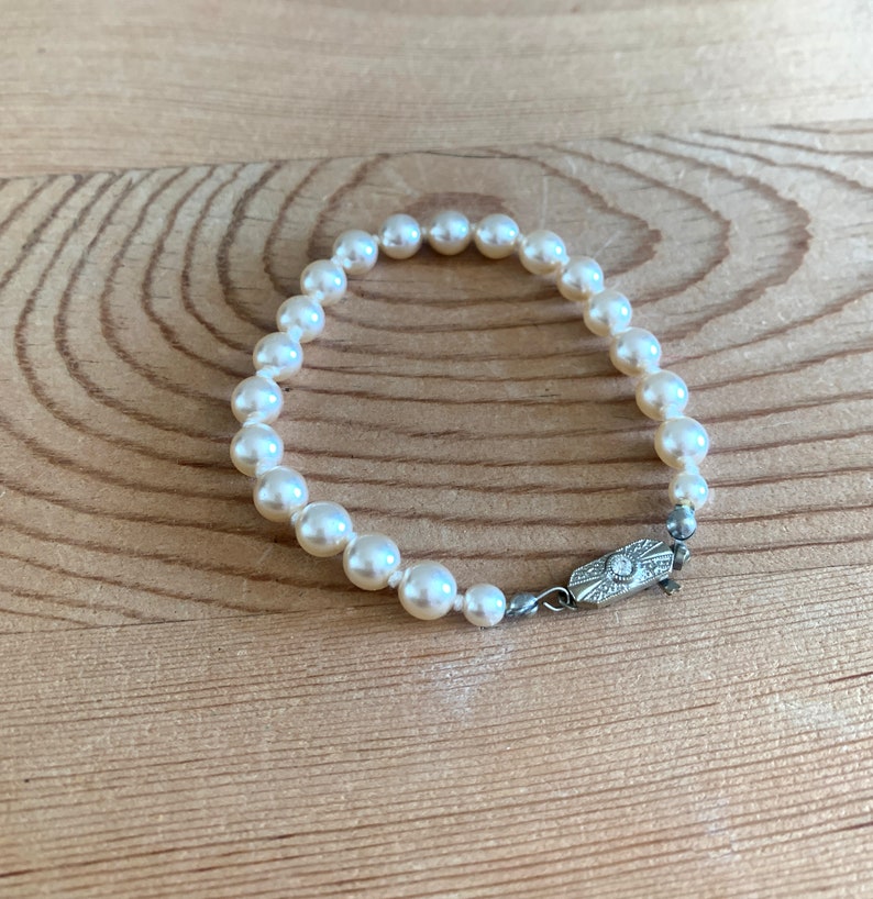 May include: A white pearl bracelet with a silver clasp. The bracelet is made of small, round pearls and has a simple design.